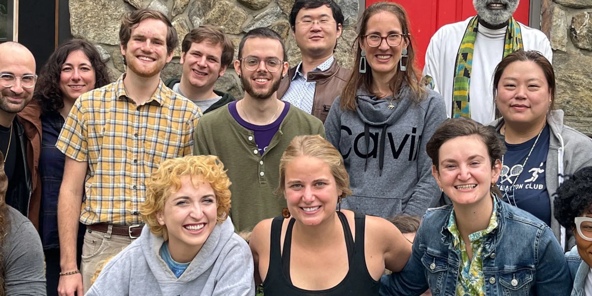 A diverse group of young adults smile while posing in front of the Chapel at Trinity Retreat Center