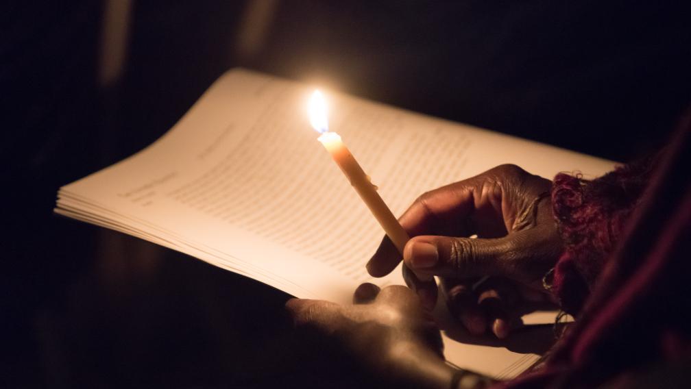 A person holds a candle to read the prayer. 
