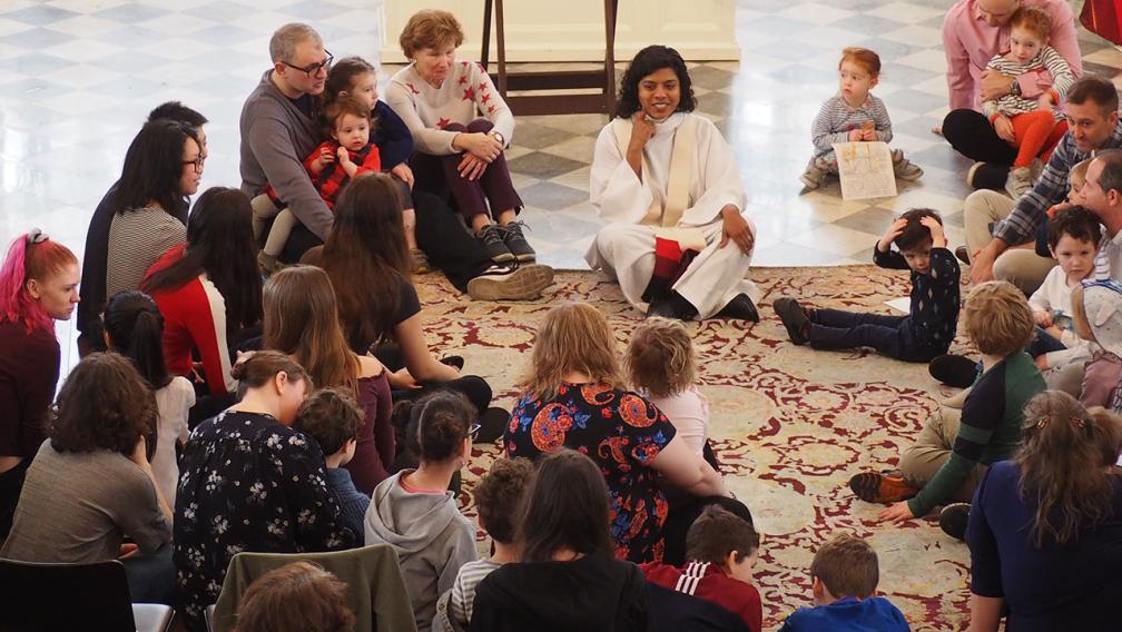 The Rev. Winnie Varghese sits on the carpet during a sermon at the 9:15 Family Service in St. Paul's Chapel, surrounded by families.
