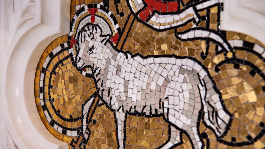 A mosaic of a lamb made up of white, gold, and red tiles on an altar