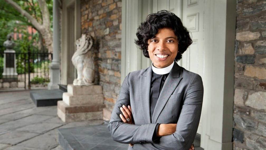 The Rev. Winnie Varghese stands on a porch in front of St. Mark's.