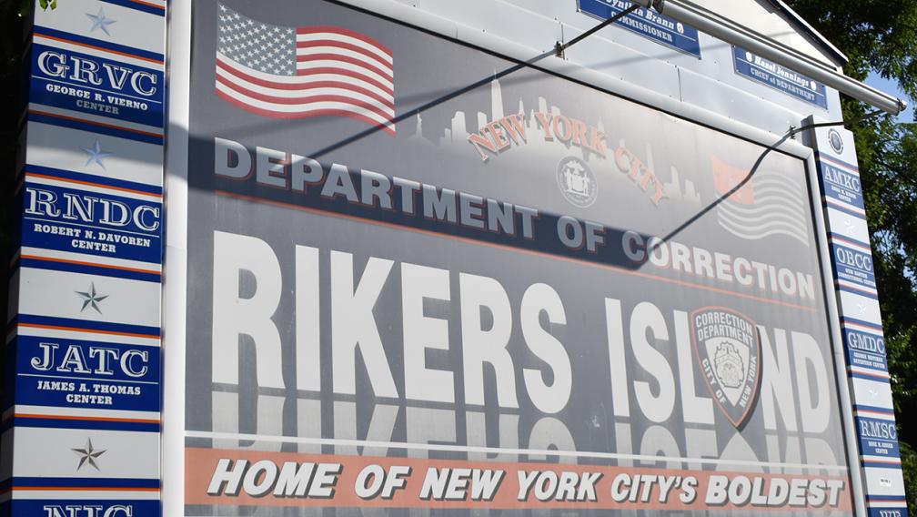A sign which reads "Department of Correction, Rikers Island. Home of New York City's Boldest"