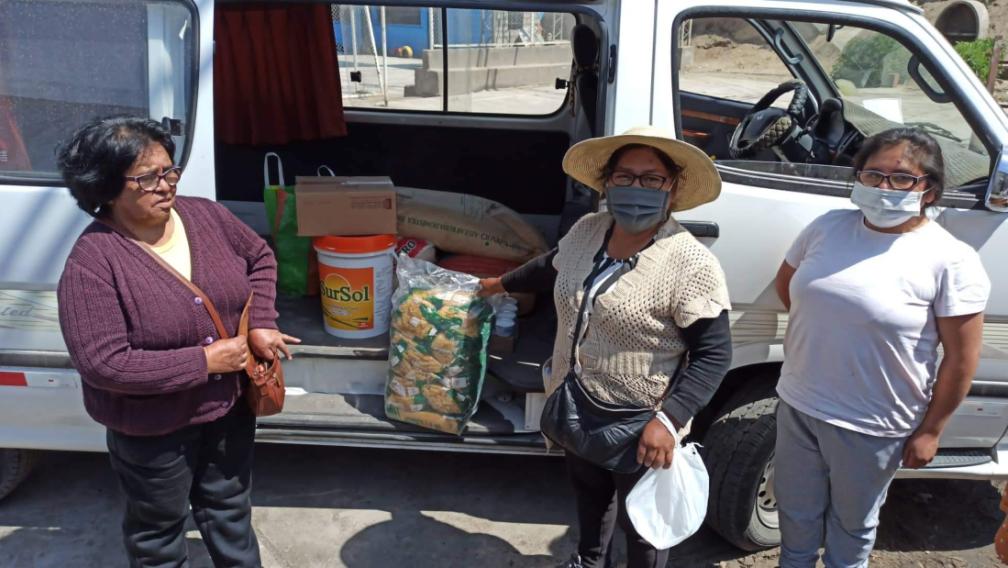 Women stand in front of a van with doors open showing food items