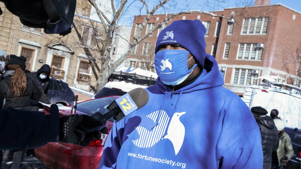 A masked representative from the Fortune Society speaks into a News12 microphone.