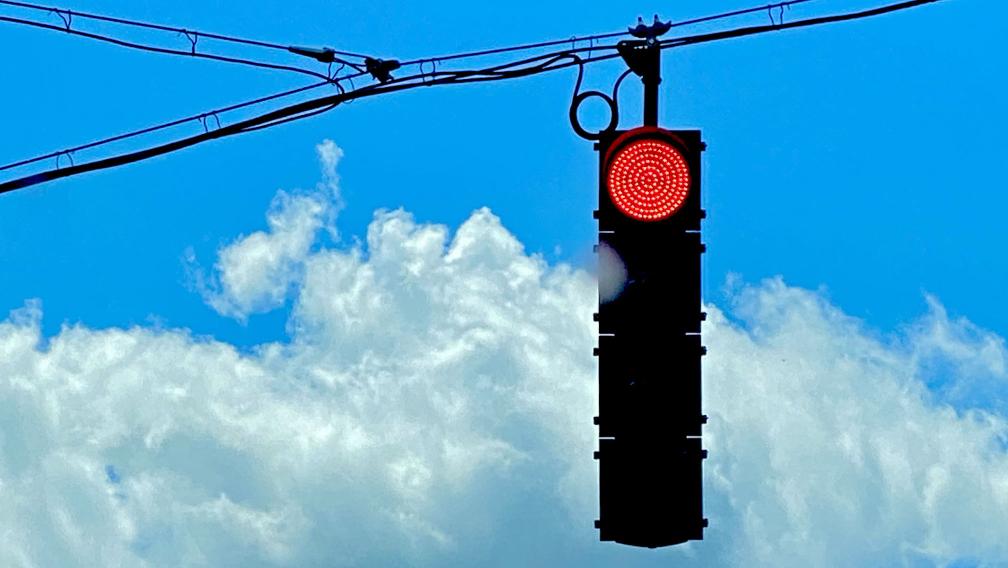 Photo of a red stoplight and a bright blue, cloud-filled sky