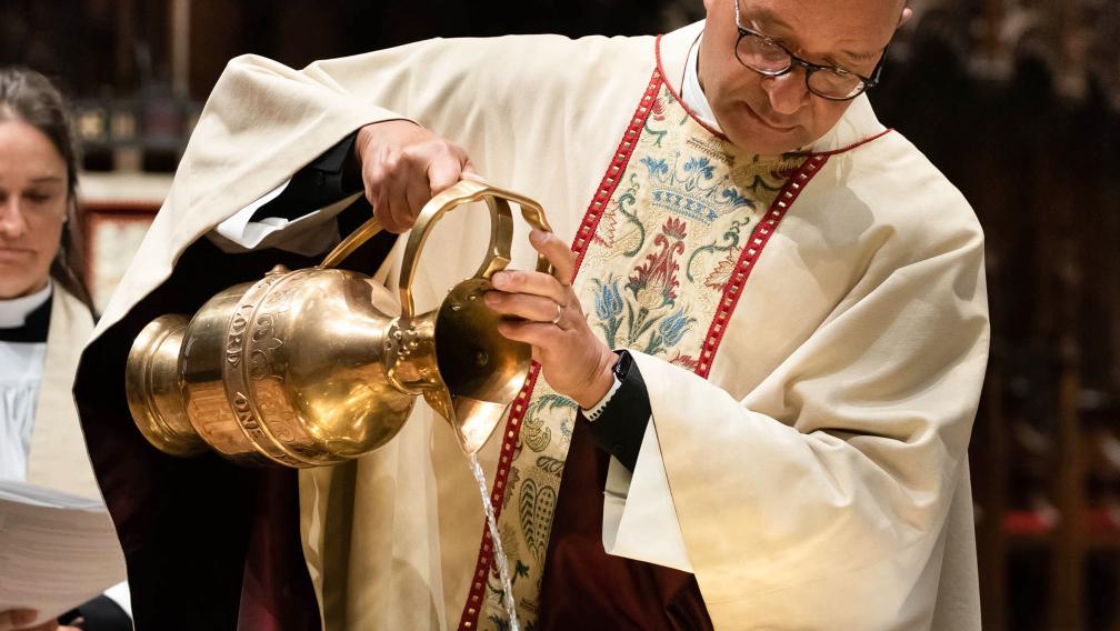 Father Phil pours water into the baptismal font in Trinity Church