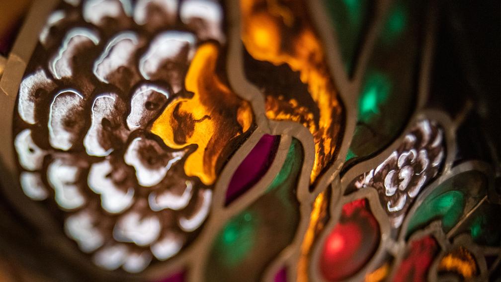Close-up photograph of a stained-glass window depicting a flower with white, gold, green, red, and burgundy