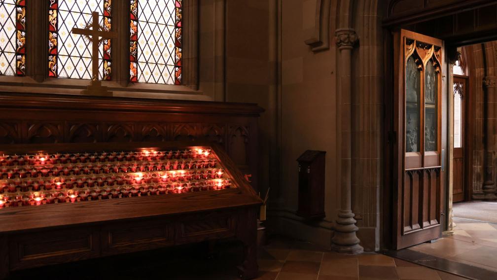 Light shines through an open door in Trinity Church and prayer candles burn beneath a stained-glasses window