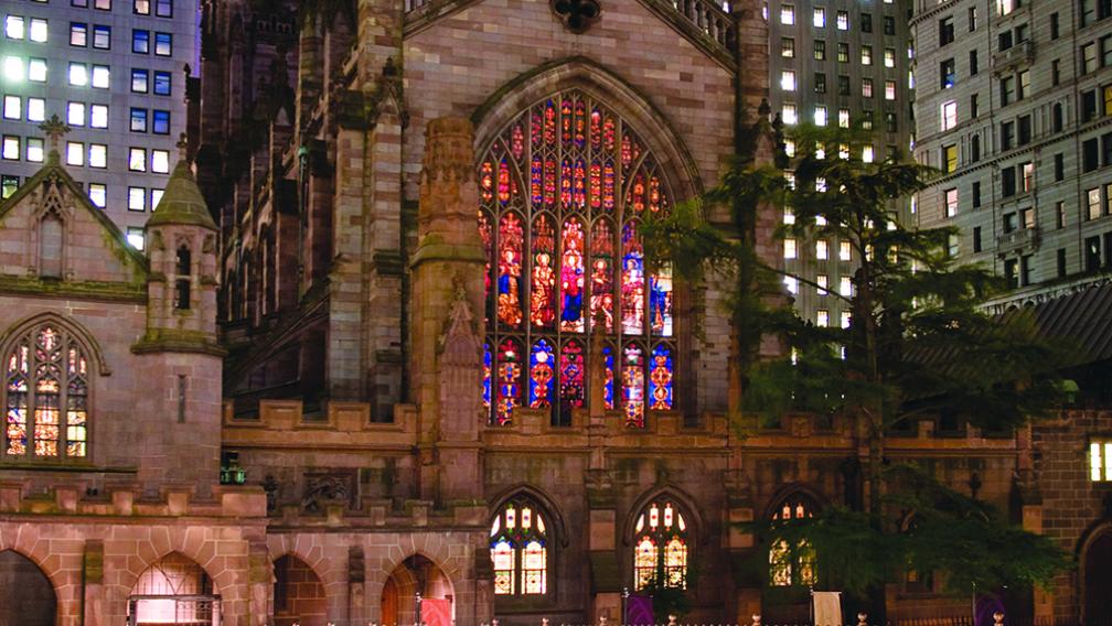 Trinity Church lit up at night with a bridge and stained glass window.