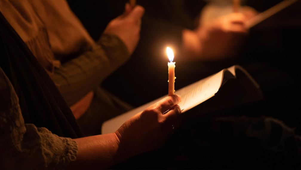 A person holds a glowing, burning candle on their hand during a vigil service at Trinity Church