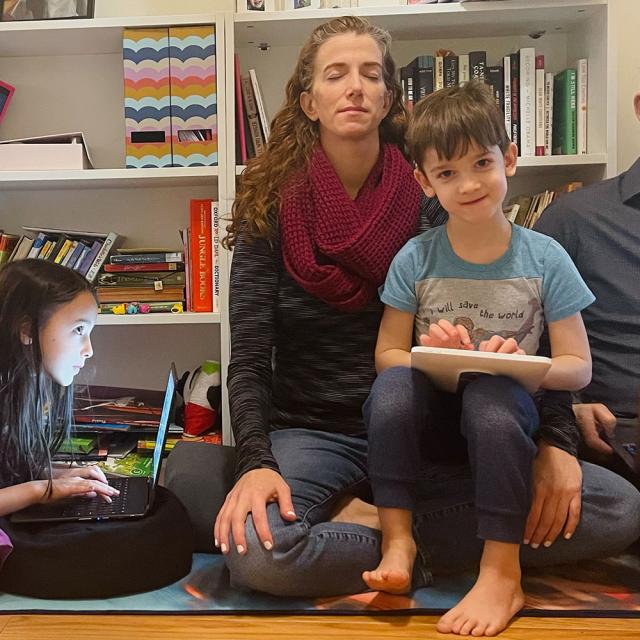 A family enjoys a variety of activities: girl plays on a computer, mom meditates, and boy types on a tablet