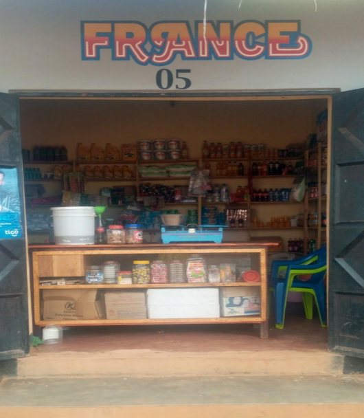 A retail stall in Biharamulo, Tanzania. The text on the sign reads "FRANCE 05." The stand is fully stocked with groceries and other supplies.