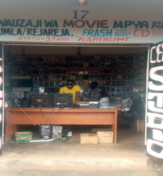 A man stands behind a counter at a retail stall in Biharamulo, Tanzania.