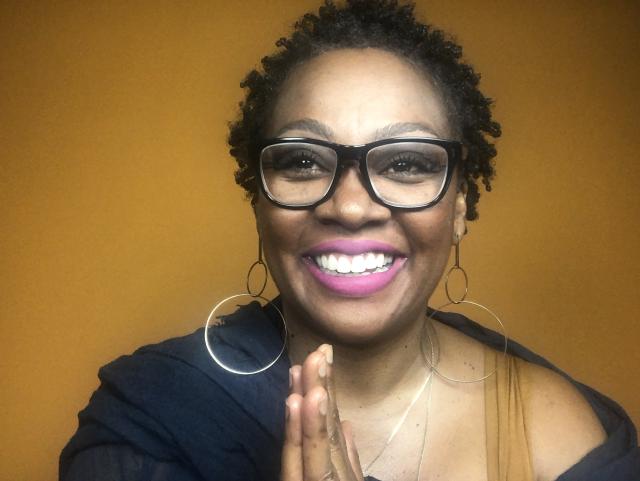 Alexus Rhone smiles directly at the camera. She's wearing hoop earrings and glasses.