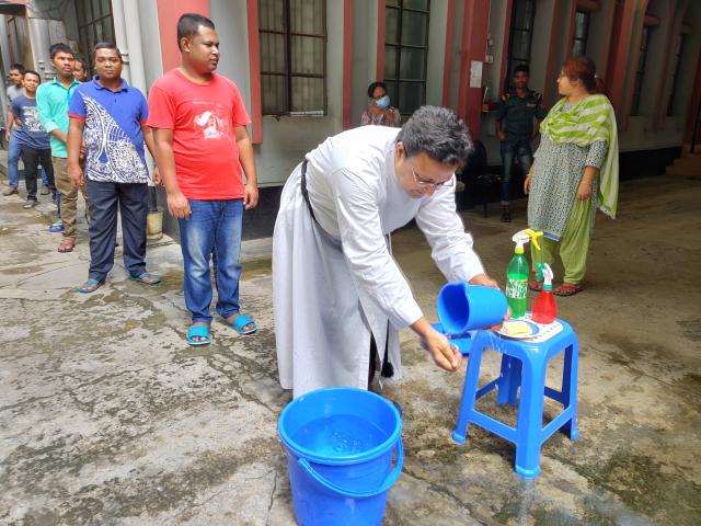A clergy person wearing white washes her hand with a bucket at a handwashing station in Bangladesh.
