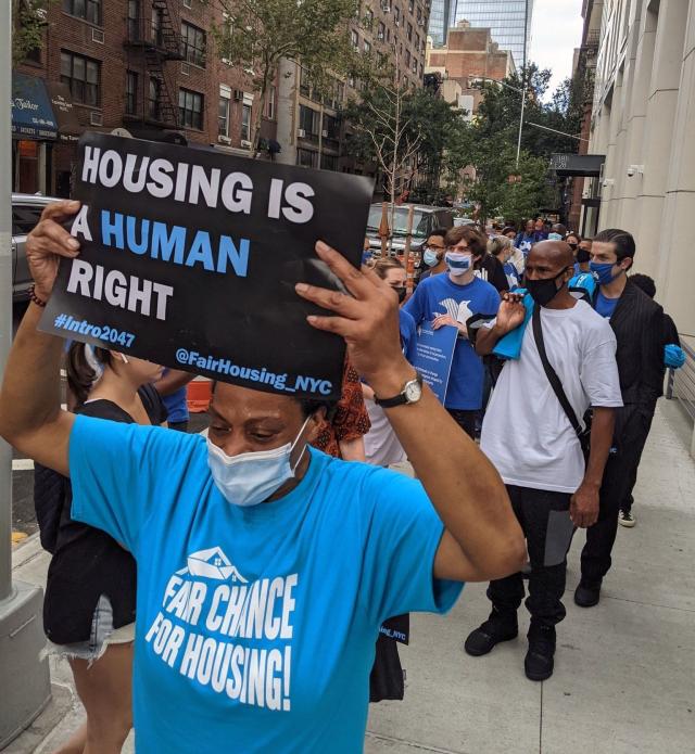 Fair Chance for Housing rally, where masked protestors hold signs reading "Housing is a Human Right."