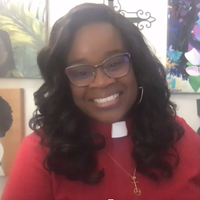 Shernell Edney Stilley smiles at the camera, wearing glasses, a red clergyperson clothes, and a gold cross necklace.