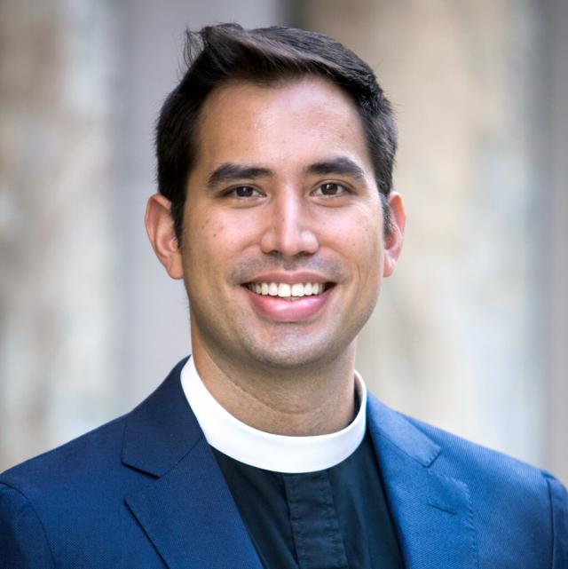 The Rev. Zack Nyein smiles at the camera, wearing a priest's collar and navy blazer.