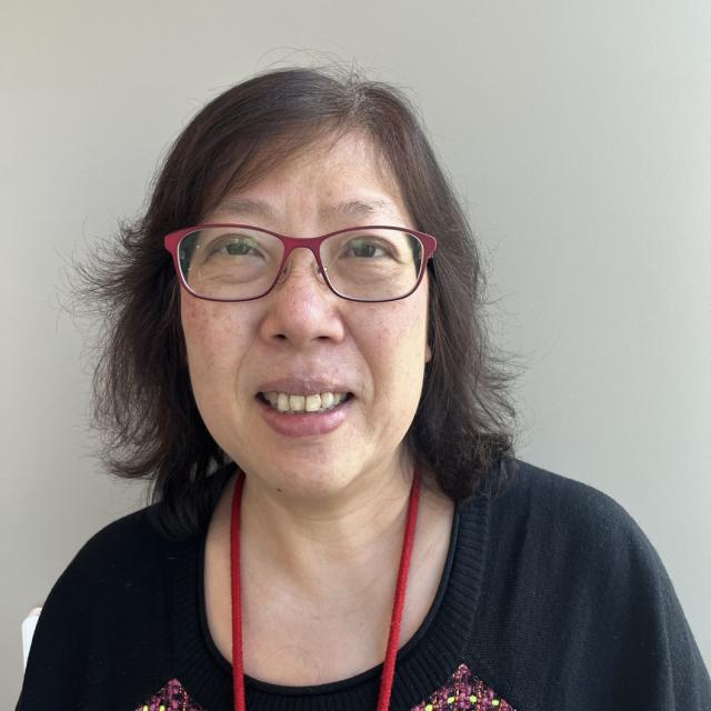 Chui Man Lai looks at the camera, wearing red glasses, a red lanyard around her neck, and a black shirt with red accents. She is of East Asian descent and has freckles.
