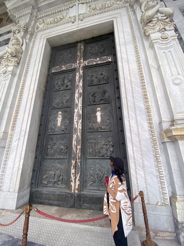 Woman stands in front of tall ornate door