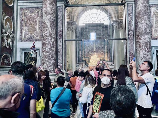 Pilgrims stand in St. Peter's Basilica, with the sculpture of a woman holding a wounded man in the background
