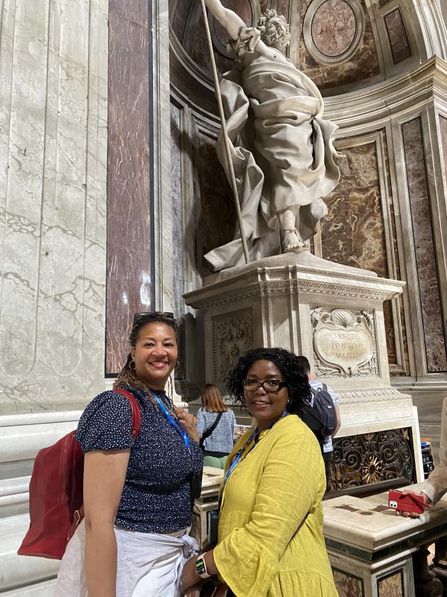 Two women stand in front of sculpture in church