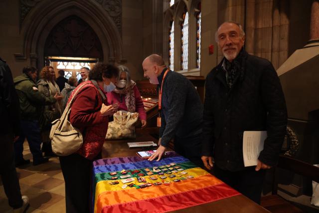 Al DiRaffaele stands behind a table with a Pride flag in the back of Trinity Church