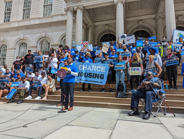 Members of the Fair Chance for Housing campaign stand on the stairs of NYC City Hall for a rally.