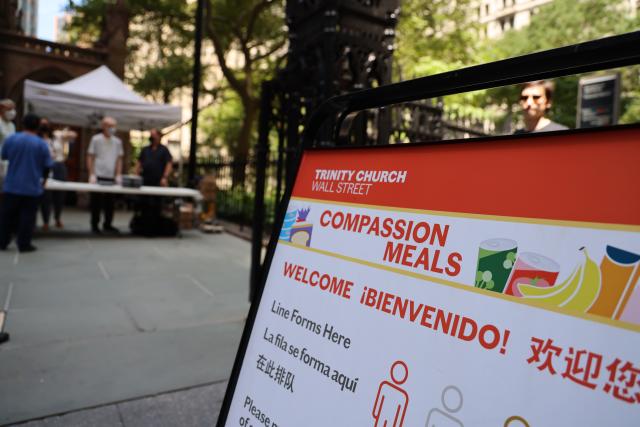 A sign reading "Compassion Meals" and "Welcome" in English, Spanish, and Chinese is shown on the sidewalk outside of Trinity Church.