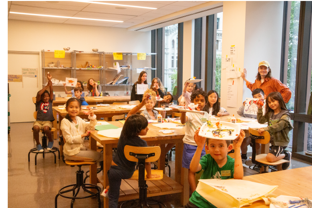 Children hold up their sculptures for the camera in the Trinity Commons art studio.