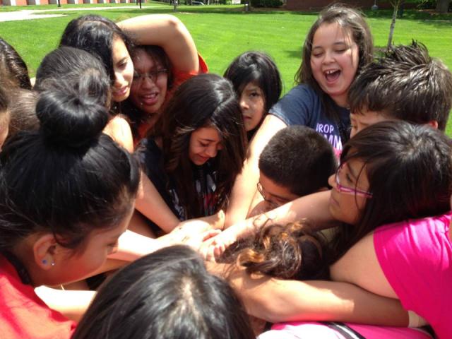 A group of students from the Hispanic Youth Leadership Academy huddle in a circle with their arms in the center.
