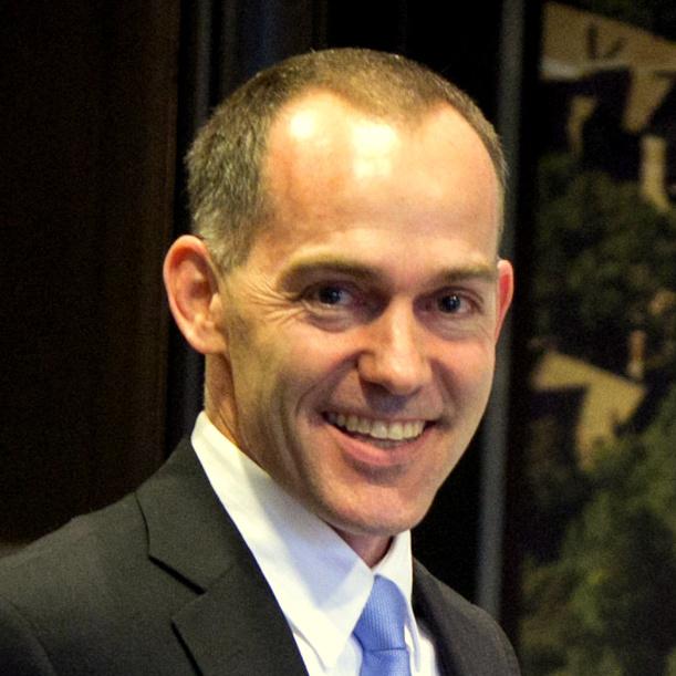 Brad Fulton smiles while wearing a dark suit and light blue tie.