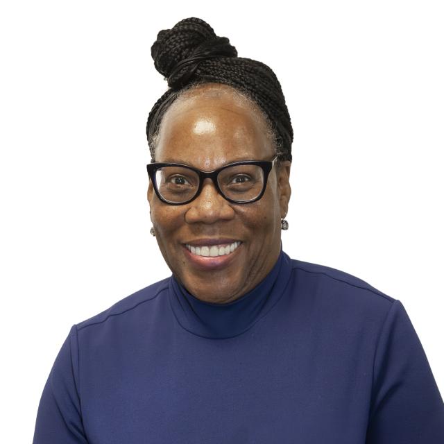 Cecilia Scott-Croff wears a blue turtle neck and black glasses. Her braided hair is up in a bun.