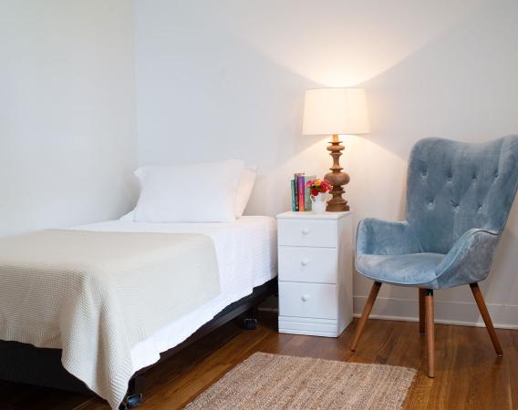Single bed, with bedside table, books, and tufted armchair