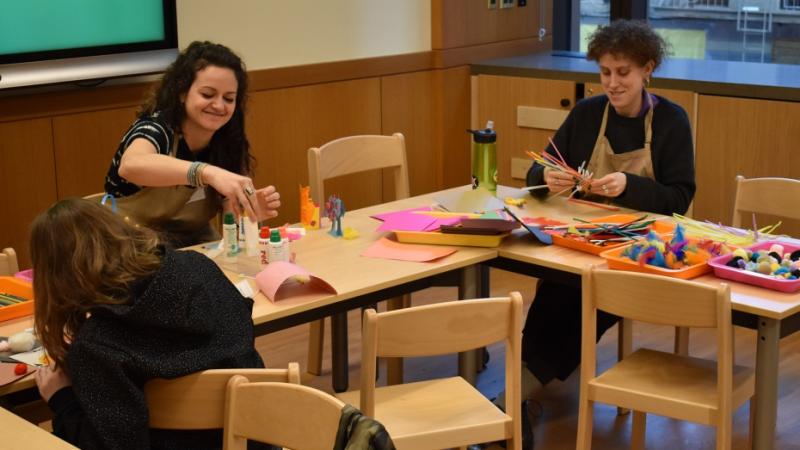 Three young women work colorful pipe cleaners and pom poms into fanciful sculptures during an art workshop.
