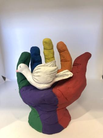 A sculpture of a rainbow-colored hand holding a white dove