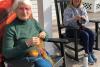 Two women knit in the rocking chairs on the porch