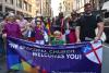 Two priests and a child hold a purple banner that says "The Episcopal Church Welcomes You!" There are other Trinity folks walking behind this banner in the 2022 Pride March in NYC.