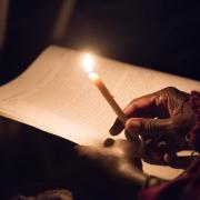 A person holds a candle to read the prayer. 