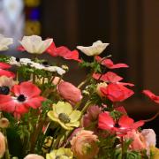 Easter flowers in Trinity Church — bright and soft pink, yellow, and white flowers with a stained glass window in the background