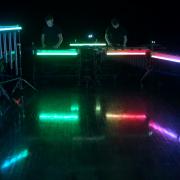 Rainbow lights in a dark space where percussionists are playing.