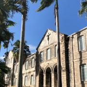An exterior shot of Codrington College in Barbados, January 2020. The palm trees in the foreground sway to the left.
