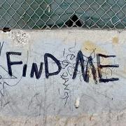 The words "Fine Me" painted in black on a cement barrier in the street