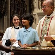 A young baptismal candidate stands at the font with Father Phil and Mother Kristin