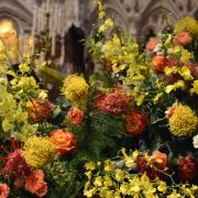 An arrangement of bright yellow and orange flowers in front of the Astor reredos in Trinity Church