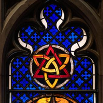 A stained glass window featuring a gold trinity knot inside a red triangle over a blue backdrop