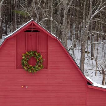 The red, wooden Retreat Center barn, decorated with a wreath, in front of snowy woods