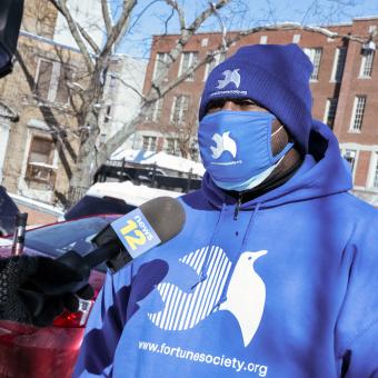 A masked representative from the Fortune Society speaks into a News12 microphone.