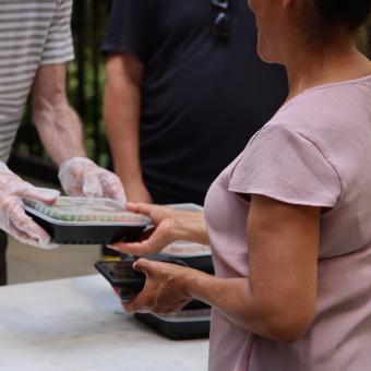 A gloved volunteer hands a Compassion Meal to a guest in Trinity Churchyard.