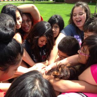 A group of students from the Hispanic Youth Leadership Academy huddle in a circle with their arms in the center.